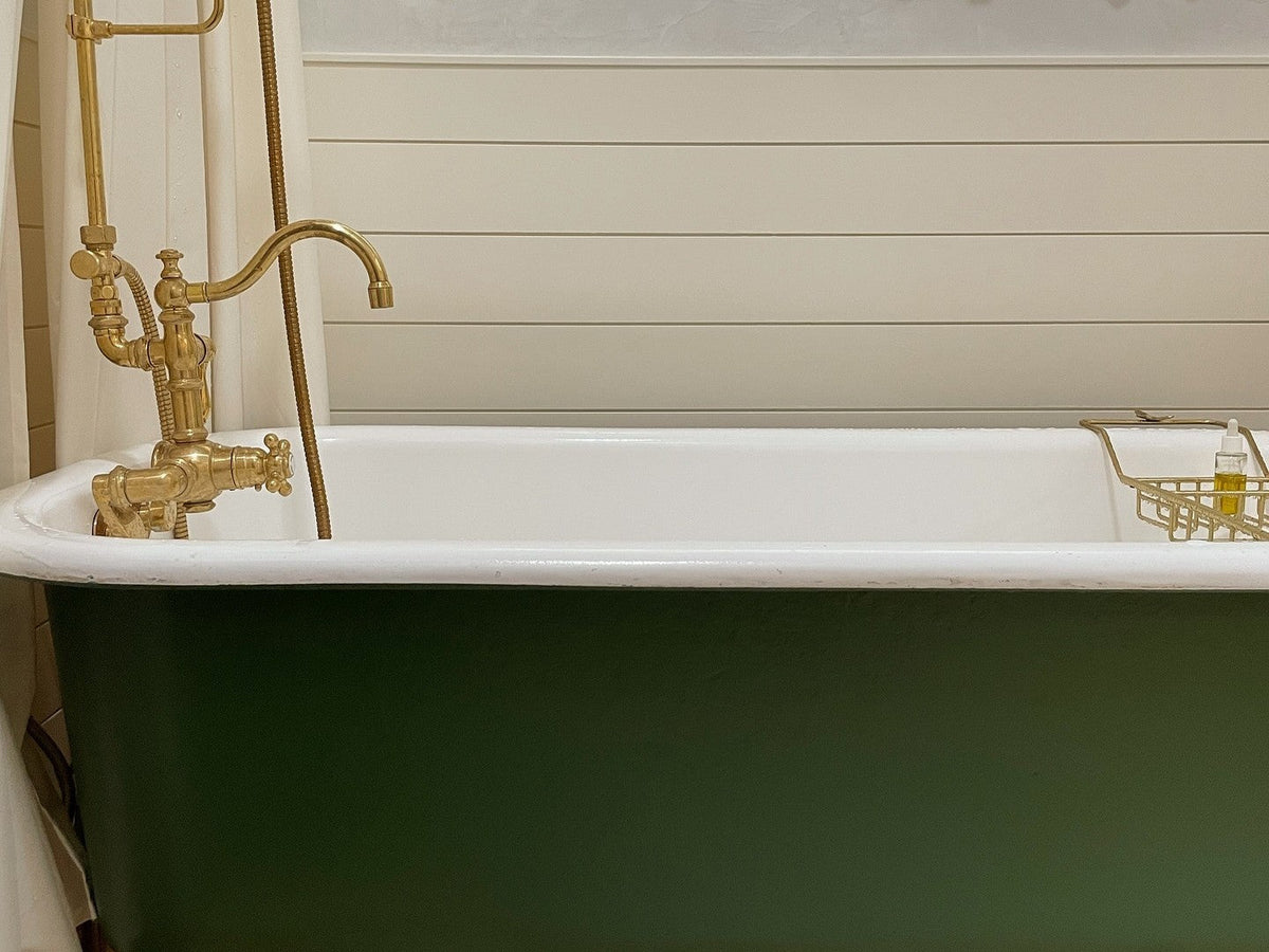 Green cast iron clawfoot tub with a brass tub filler and handheld shower in a shiplap bathroom