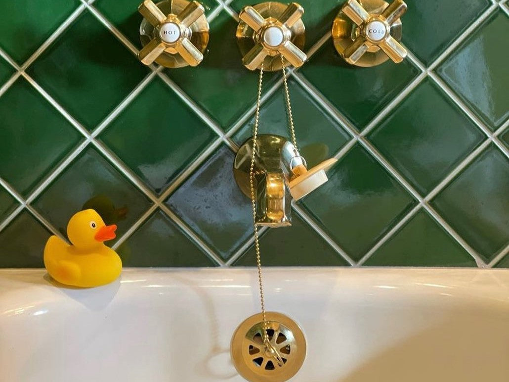 Brass tub drain, overflow and cross handles on green tile