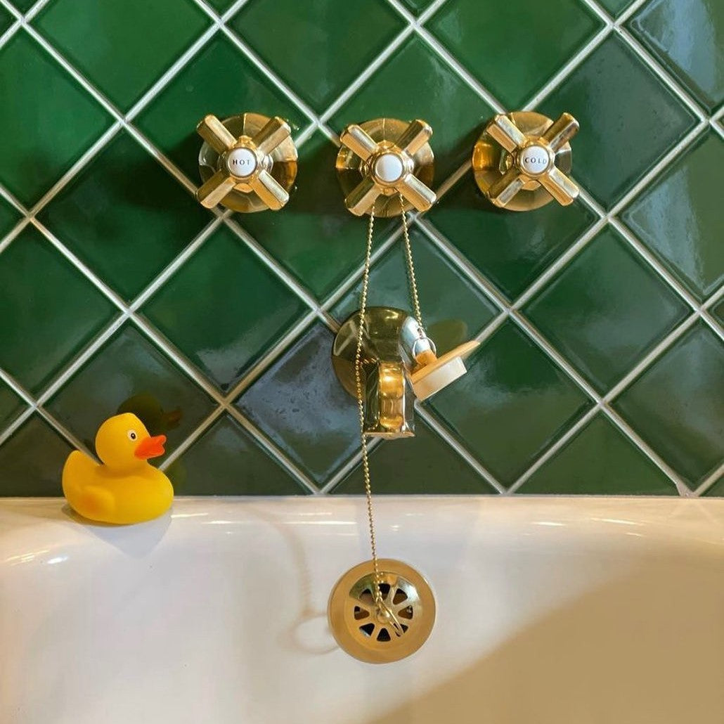 Brass tub drain and cross handles on green tile